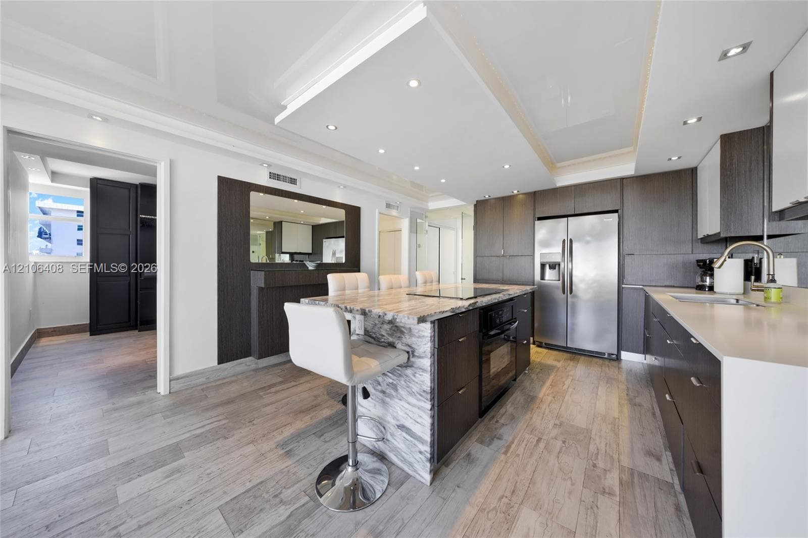 Kitchen featuring high-gloss cabinetry, stone-topped island with integrated cooktop, wood-finish flooring, and recessed ceiling lighting