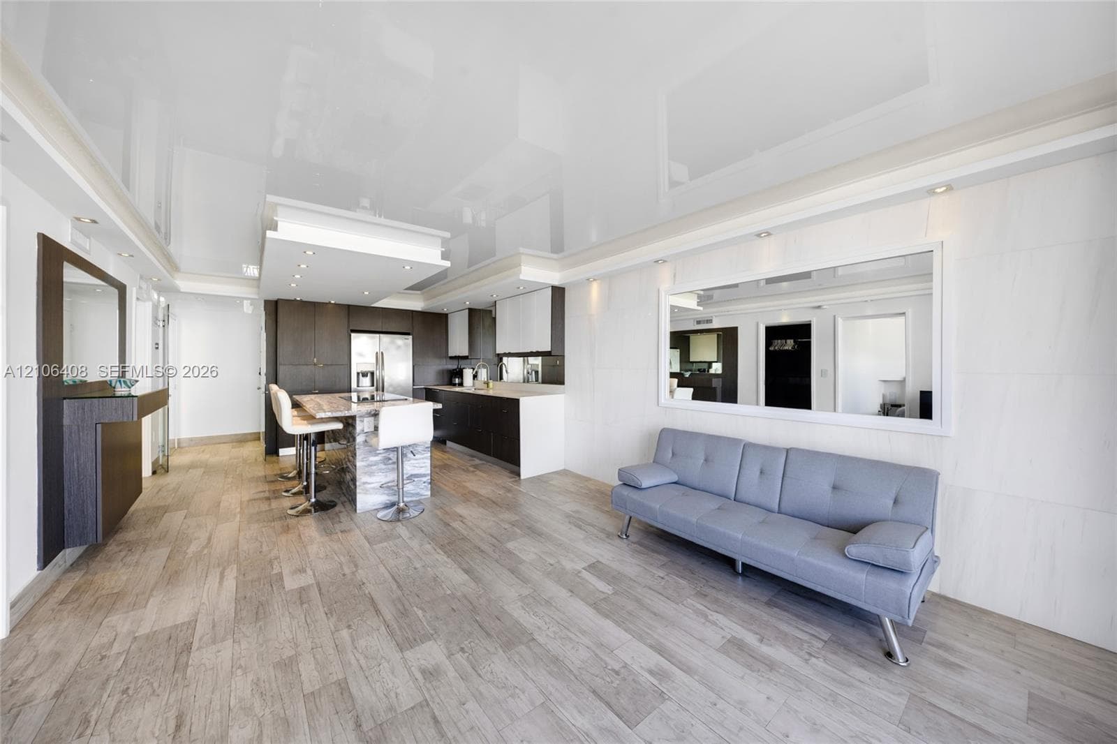 High-gloss stretch ceiling featuring recessed lighting, wood-finish flooring, two-tone cabinetry, a stone-surround kitchen island, and a large wall-mounted mirror