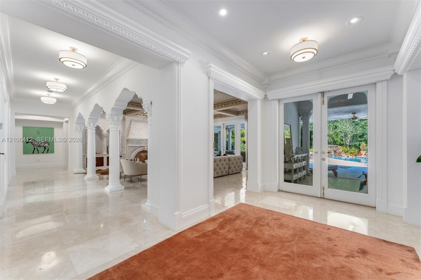 Grand foyer featuring polished stone flooring, intricate crown molding, arched architectural columns, and glass-paneled double entry doors