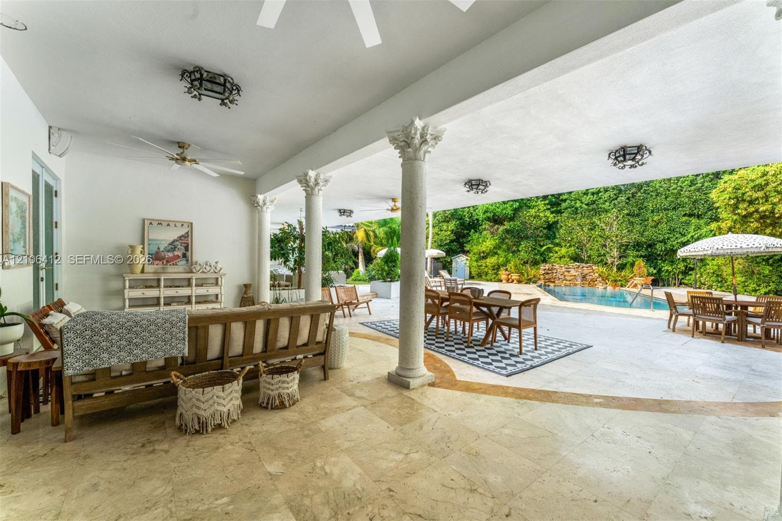 Covered patio featuring stone tile flooring, structural columns with ornate capitals, recessed ceiling lighting, and a pool with a rock water feature