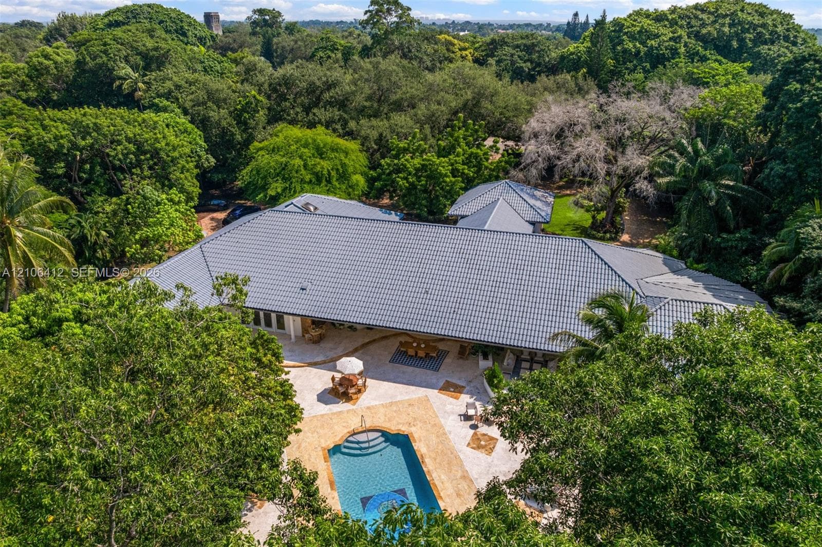 Aerial perspective of a residence featuring a multi-pitched roof, stone-paved patio, and a swimming pool surrounded by established trees