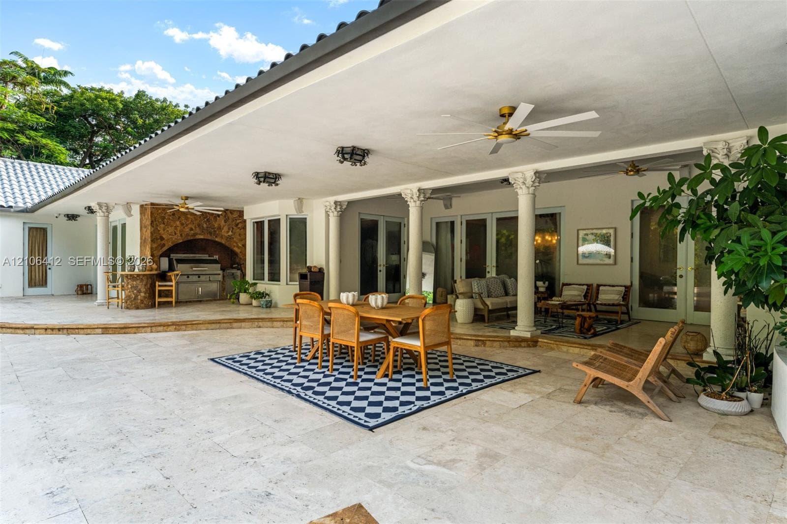 Covered patio featuring stone-tile flooring, decorative classical columns, a built-in outdoor kitchen, and dual ceiling fans