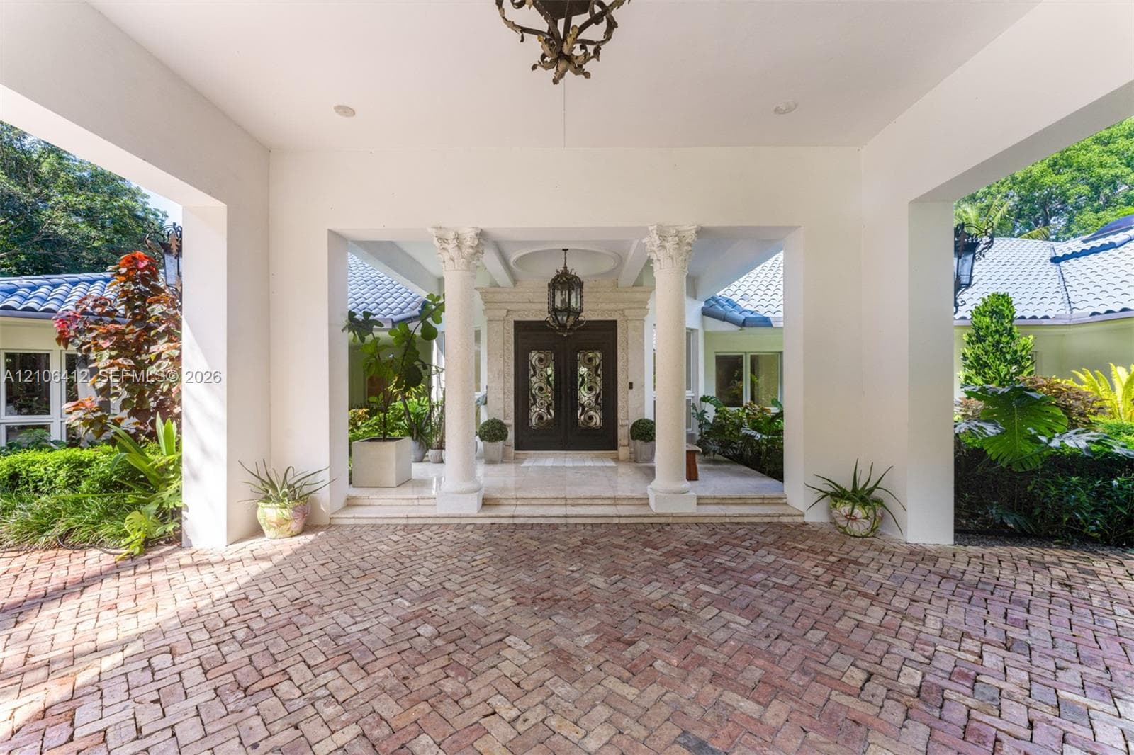 Covered motor court featuring herringbone-patterned brick paving, decorative classical columns, and dual entry doors with intricate metal detailing