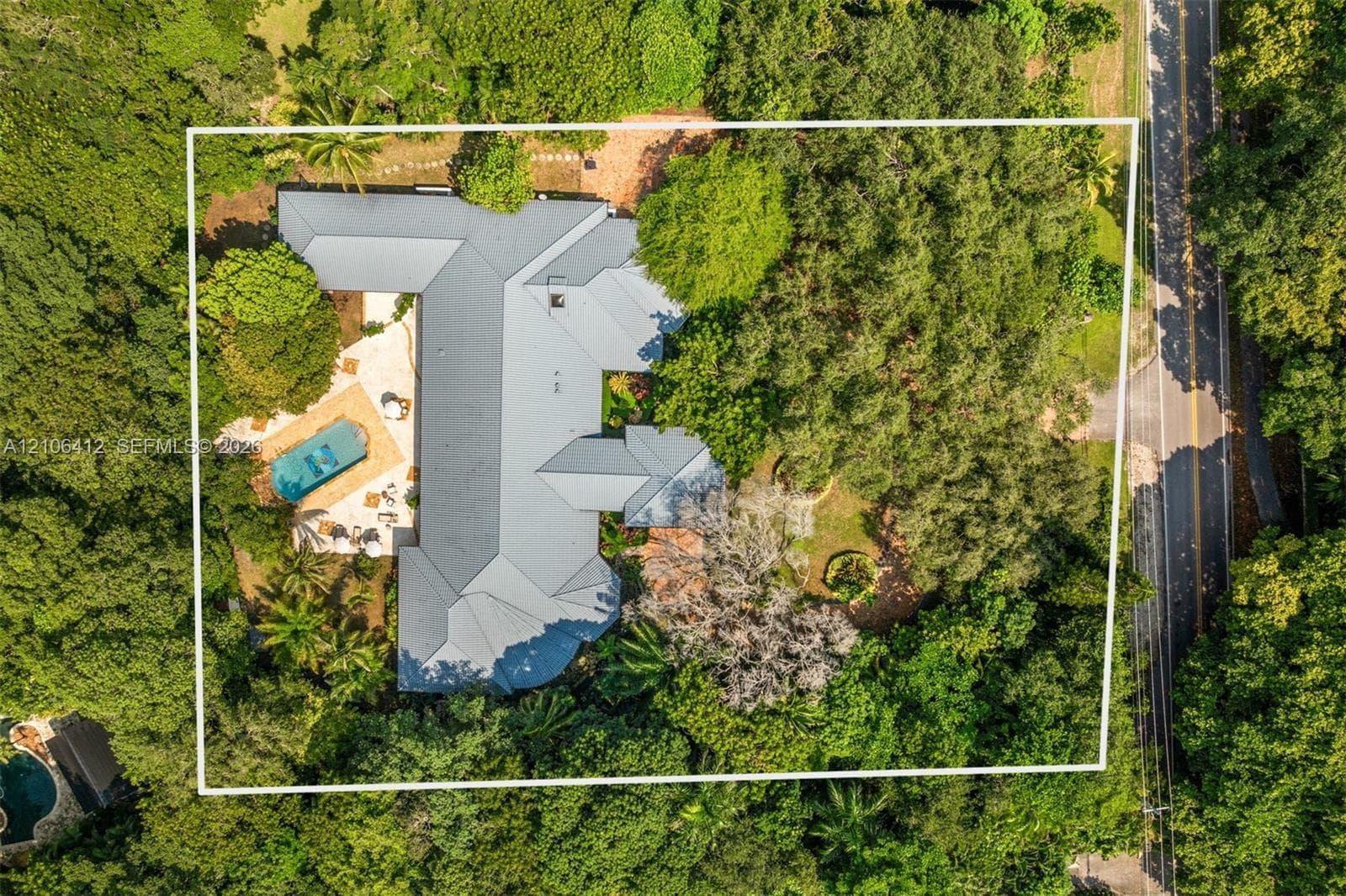 Aerial perspective featuring a metal roof, swimming pool, concrete patio, and mature trees situated on a wooded lot