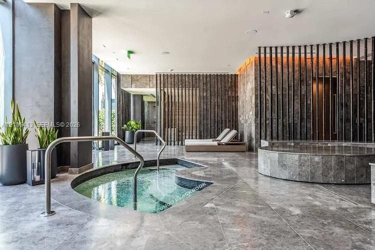 Indoor spa area featuring a built-in jetted tub with stainless steel handrails, circular cold plunge, floor-to-ceiling stone wall cladding, and vertical slat partitions