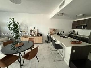 Kitchen featuring an island with a stone-finish countertop, dual-tone cabinetry, a built-in microwave, and large-format tile flooring