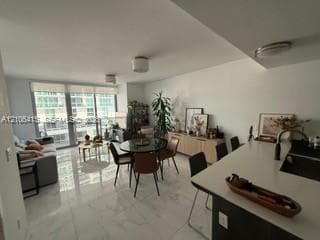 Open-concept interior featuring large-format stone-finish flooring, floor-to-ceiling glass sliding doors, and a kitchen island with stone-finish countertops and a dark-finish base