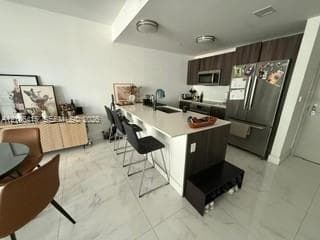 Kitchen featuring a center island with a stone-finish countertop, dark wood-finish cabinetry, stainless steel appliances, and tile flooring