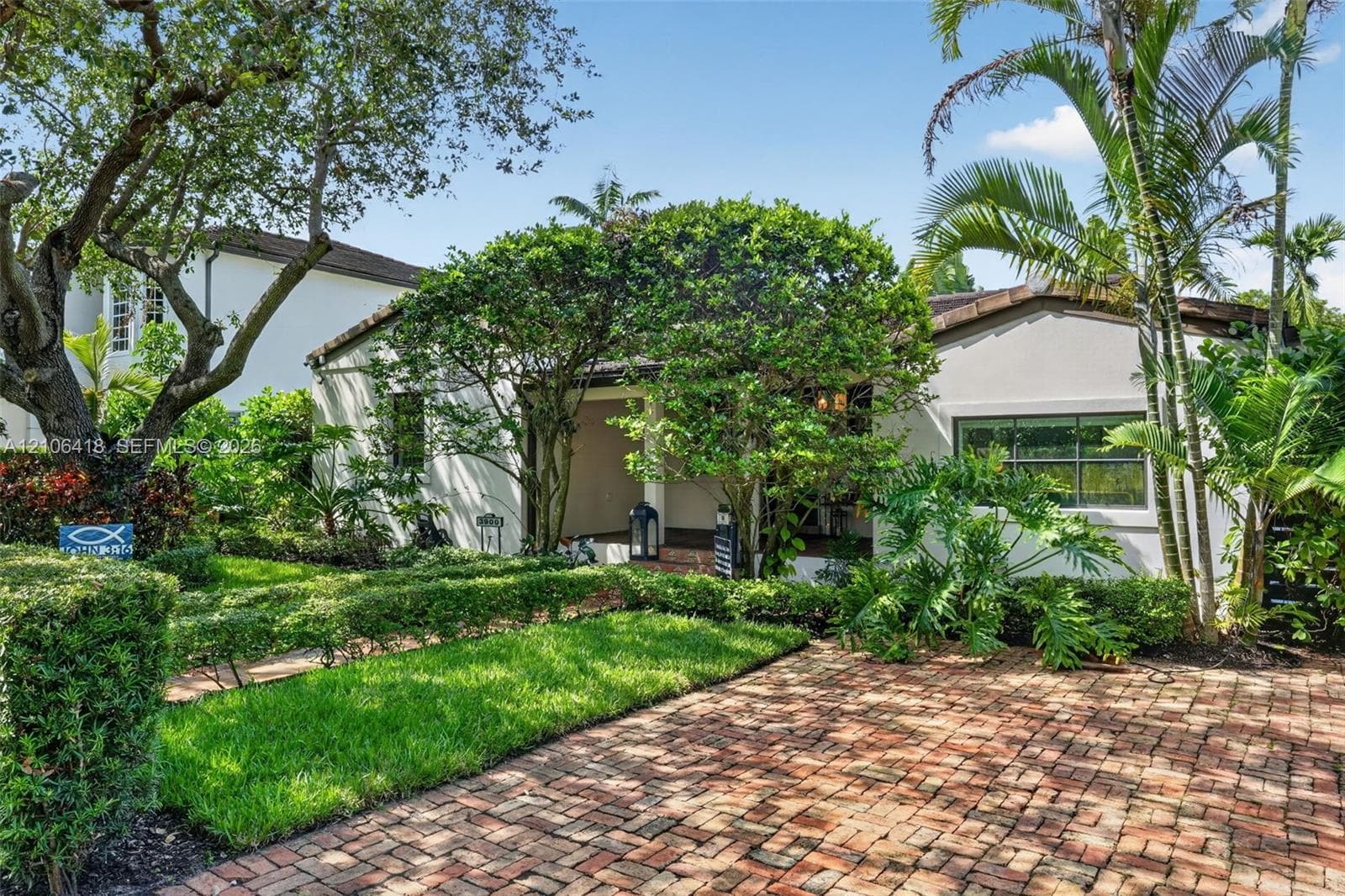 Stucco exterior featuring a brick-paved driveway, covered entrance, and mature landscaping