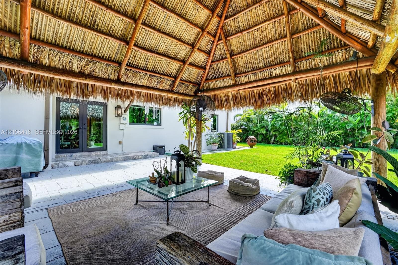 Covered outdoor pavilion featuring a natural thatched roof, timber support beams, stone-tiled patio flooring, and wall-mounted exterior lighting