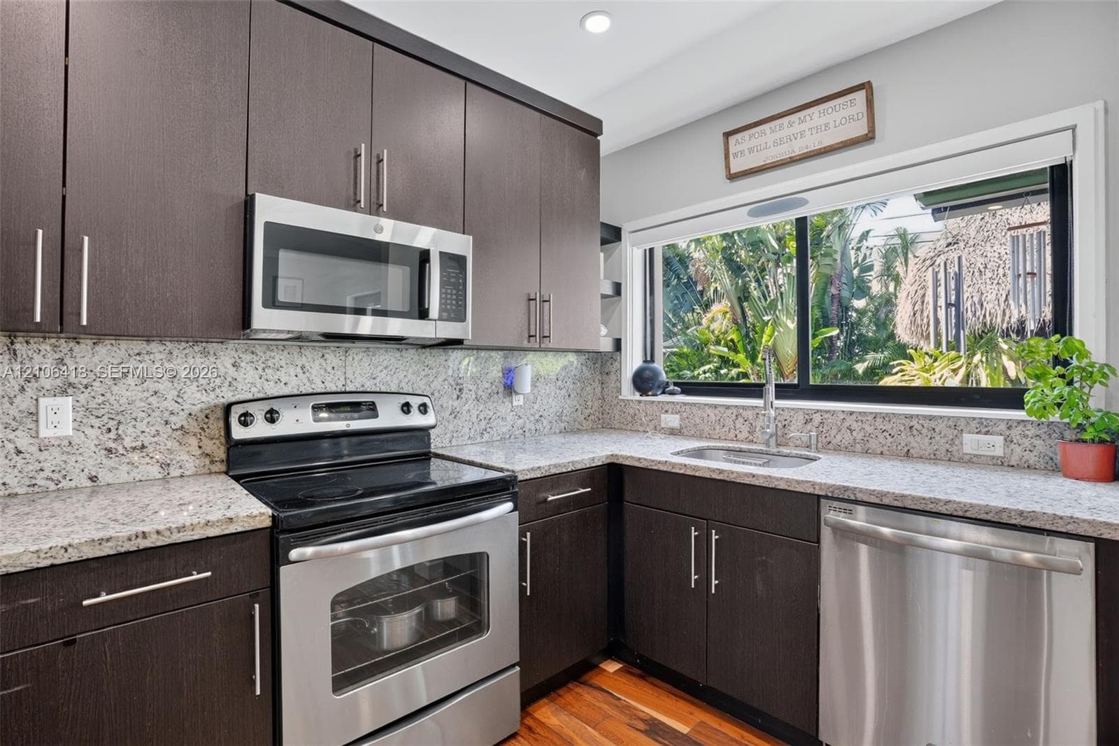 Dark-finish cabinetry featuring brushed nickel pulls, speckled stone-surface countertops, full-height stone backsplash, stainless steel appliances, and wood-finish flooring