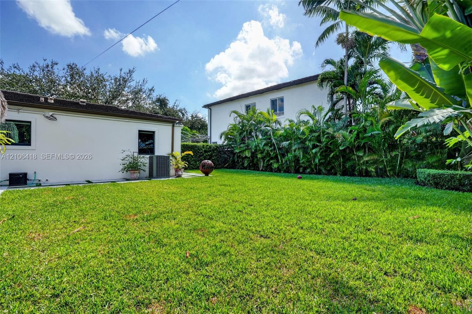 Expansive backyard featuring a lush grass lawn, mature tropical landscaping, and a paved walkway