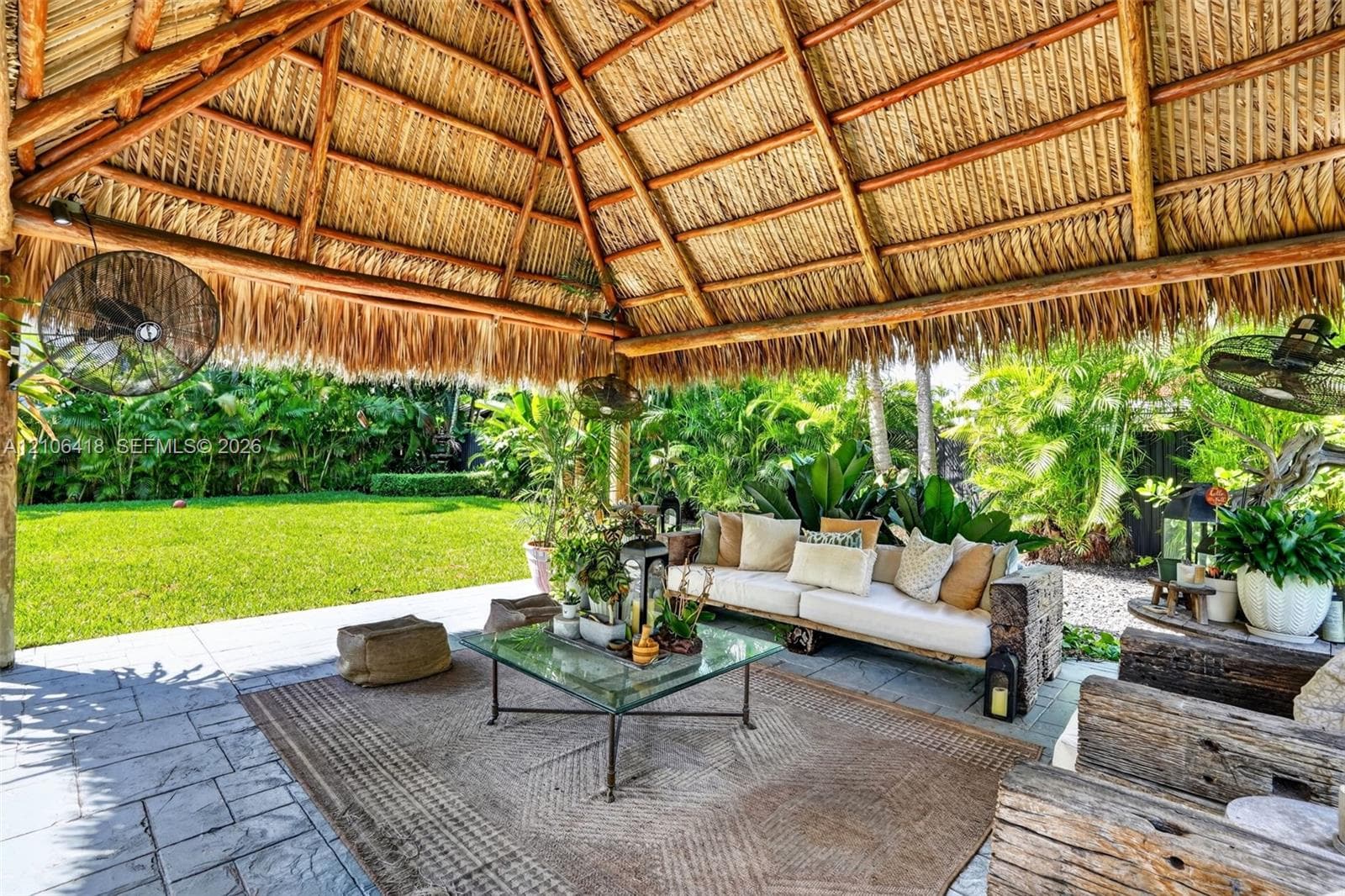 Open-air pavilion featuring a thatched roof, timber framing, integrated ceiling fans, and stone-finish patio flooring