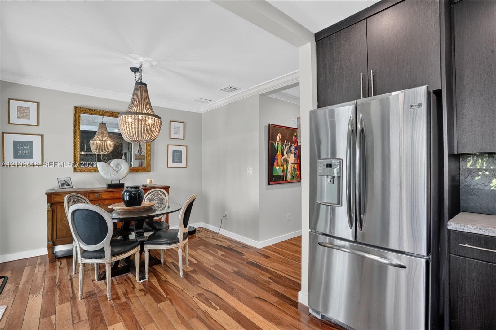 Wood-finish flooring, dark cabinetry, stainless steel refrigerator, and hanging beaded light fixture