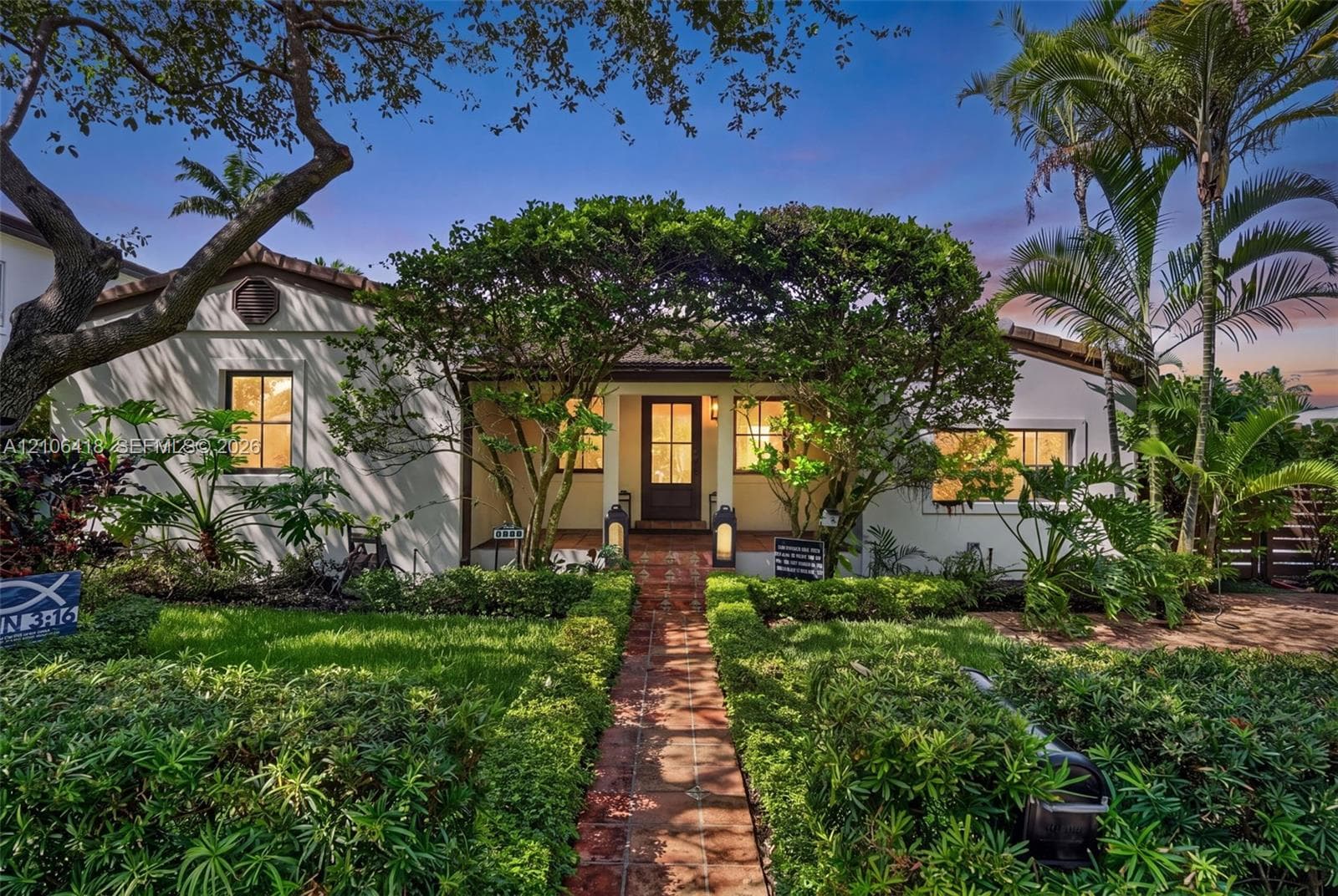 Stucco exterior featuring a tiled roof, covered entryway with a terracotta-tiled path, multi-pane windows, and manicured landscaping