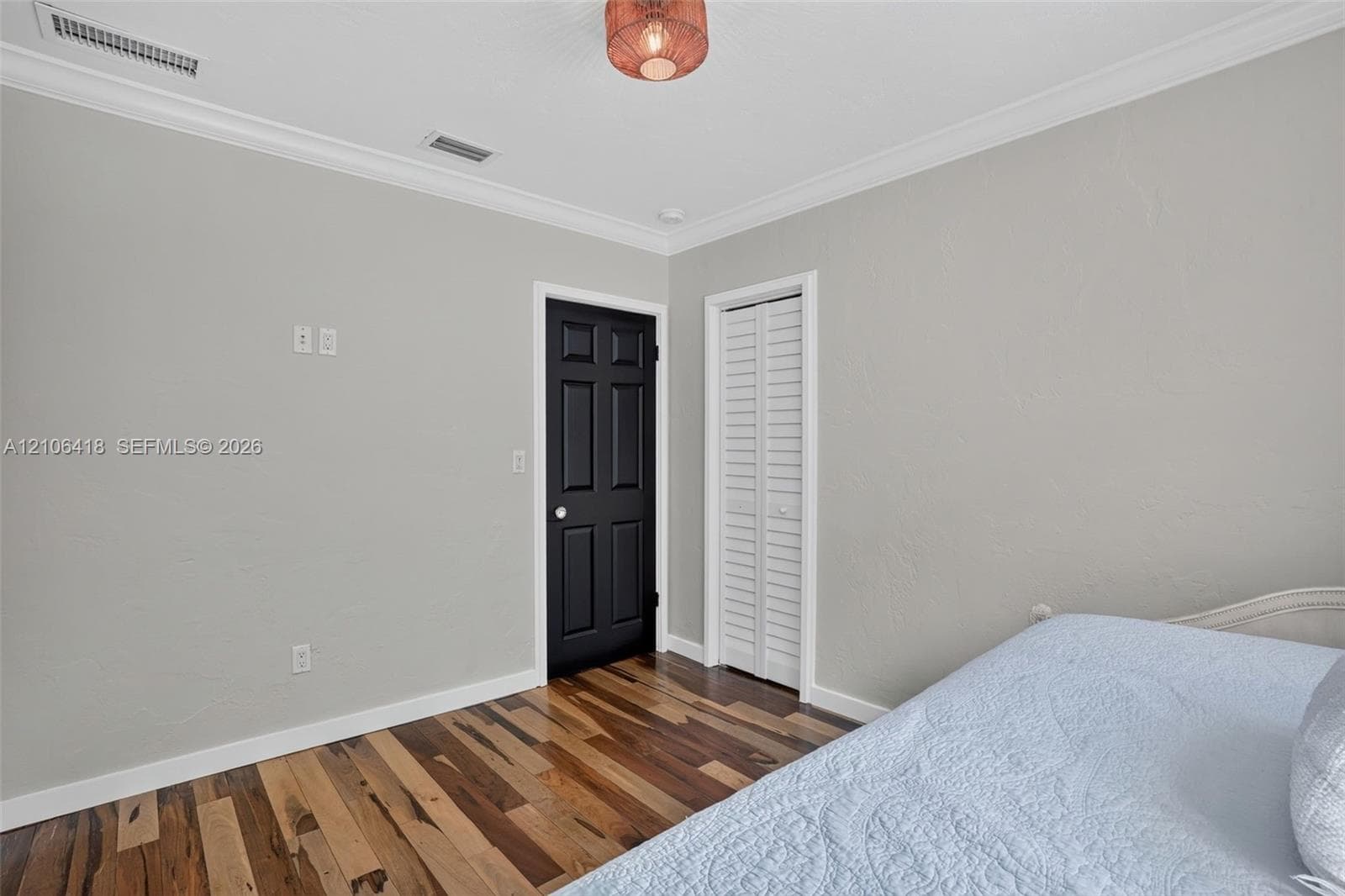 Room featuring wood-finish flooring, crown molding, a multi-panel door with matte black finish, a louvered closet door, and a decorative ceiling light fixture