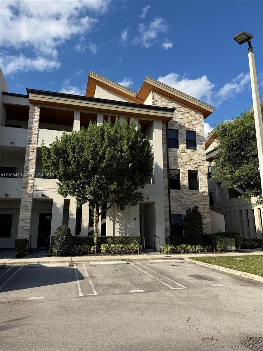 Multi-story exterior featuring stone veneer siding, split-pitch roofline, covered balconies, and paved parking area