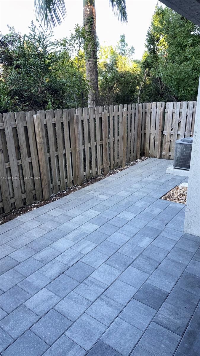 Private rear patio featuring grey stone pavers, vertical wood privacy fencing, and mature perimeter trees