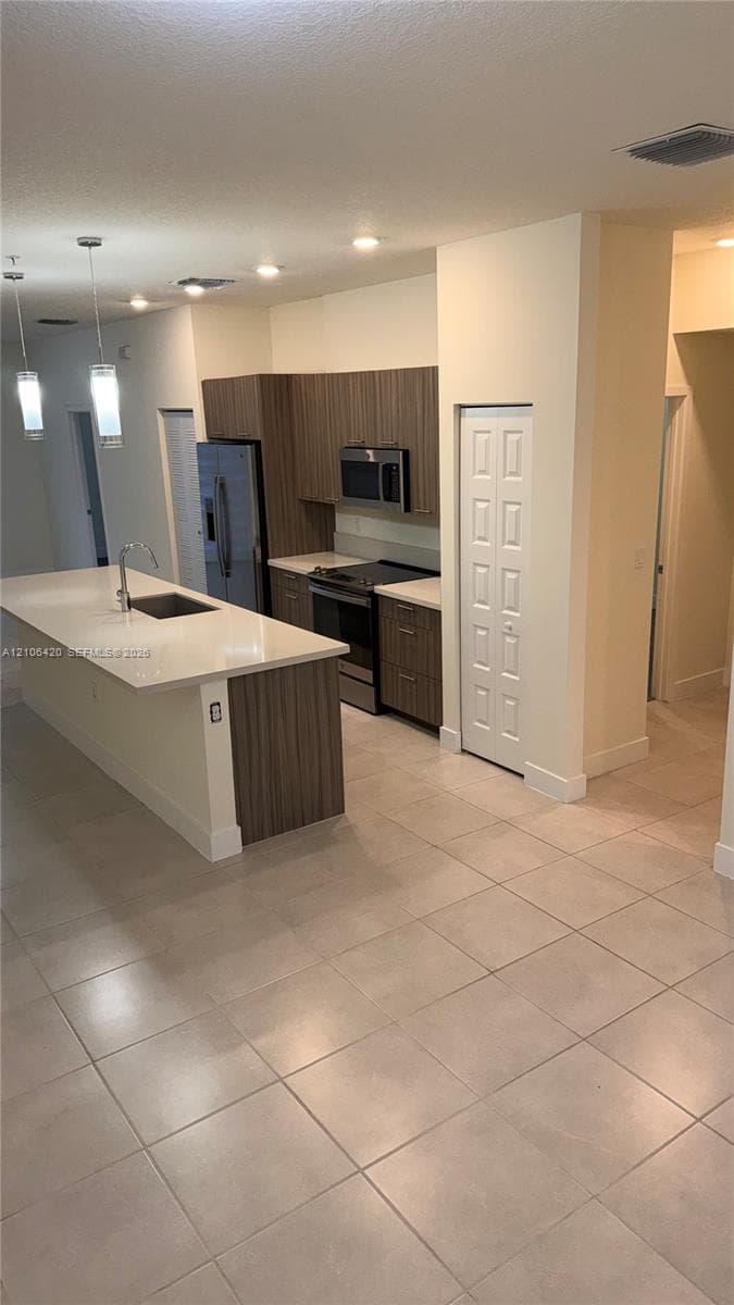 Kitchen featuring a central island with a solid-surface countertop, flat-panel cabinetry, stainless steel appliances, and large-format tile flooring