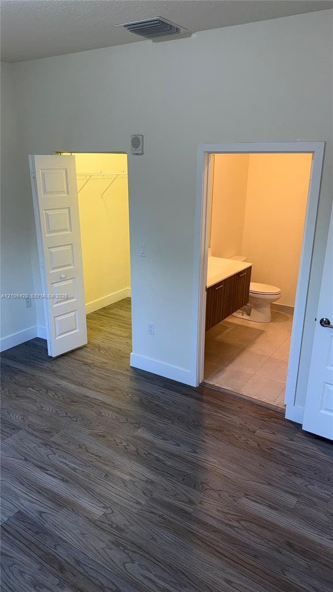 Wood-finish flooring, walk-in closet with integrated shelving, and bathroom featuring a wall-mounted vanity