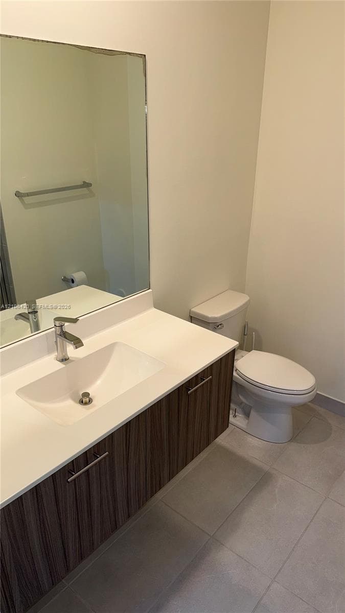 Floating vanity featuring a wood-finish cabinet, solid surface countertop with an integrated rectangular sink, wall-mounted mirror, and large-format tile flooring