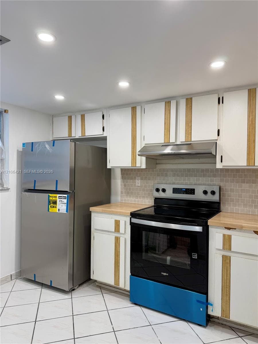 Kitchen featuring white cabinetry with wood-finish vertical accents, butcher-block countertops, a tiled backsplash, stainless steel appliances, and diagonal tile flooring