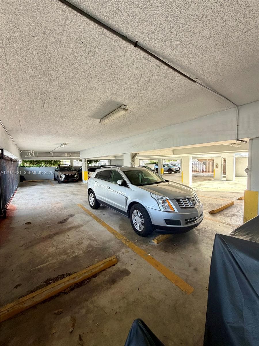 Covered parking area featuring concrete flooring, structural support columns, and surface-mounted lighting fixtures