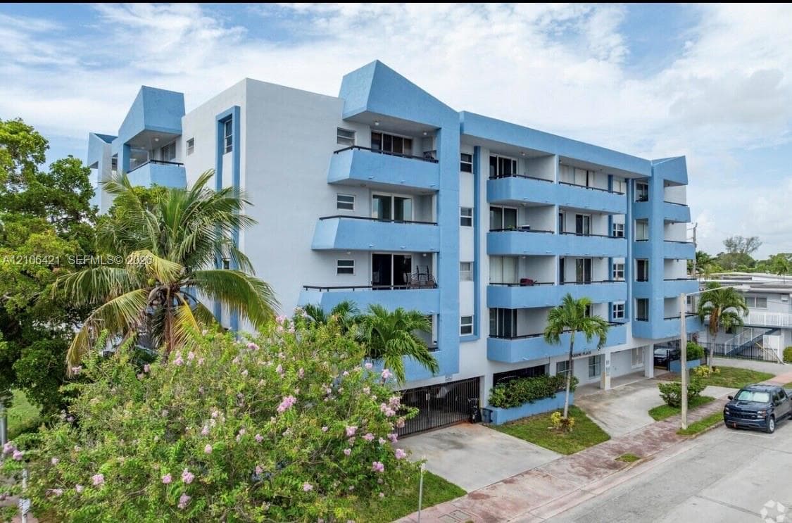 Mid-rise multi-unit residential building featuring a blue and white facade, private balconies, and gated ground-level parking