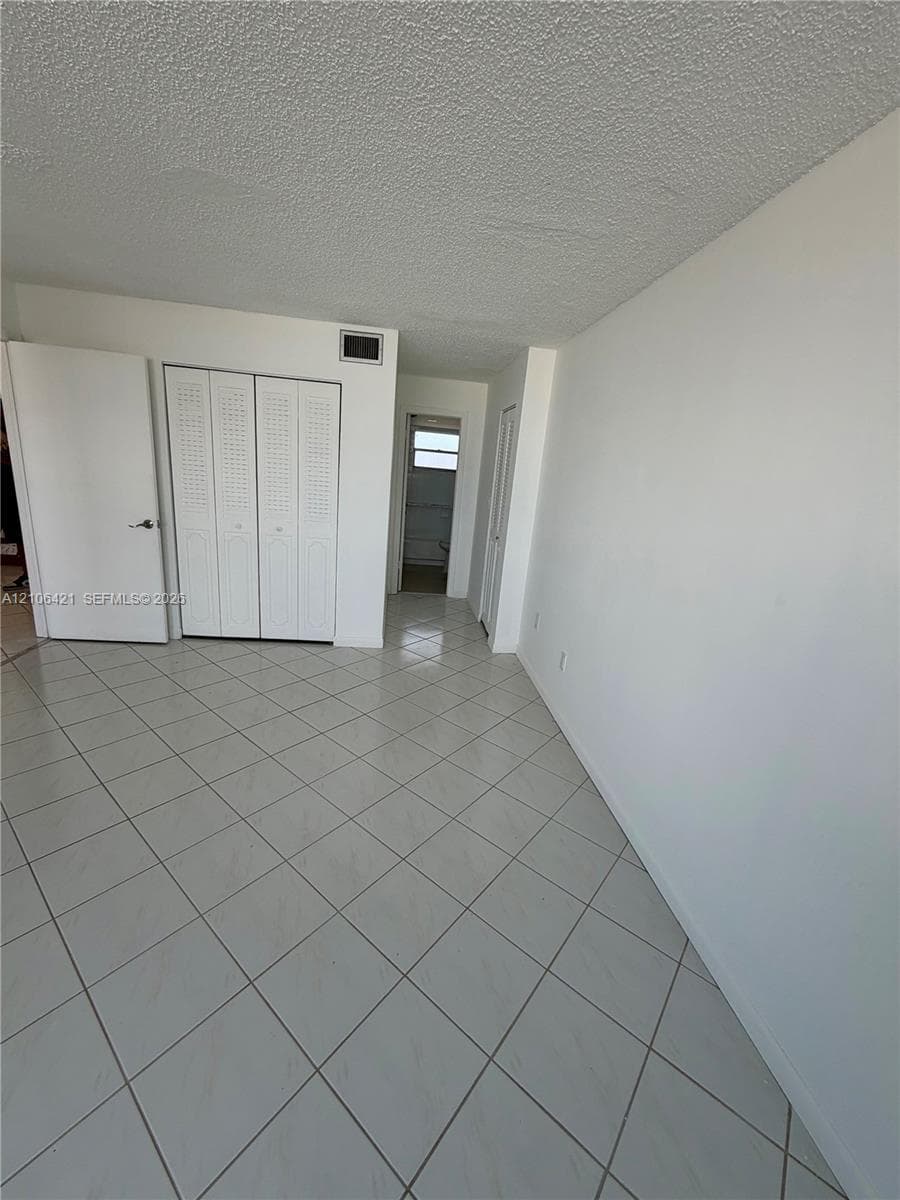 Neutral-toned tile flooring set in a diagonal pattern, white walls, and built-in closet storage with louvered doors