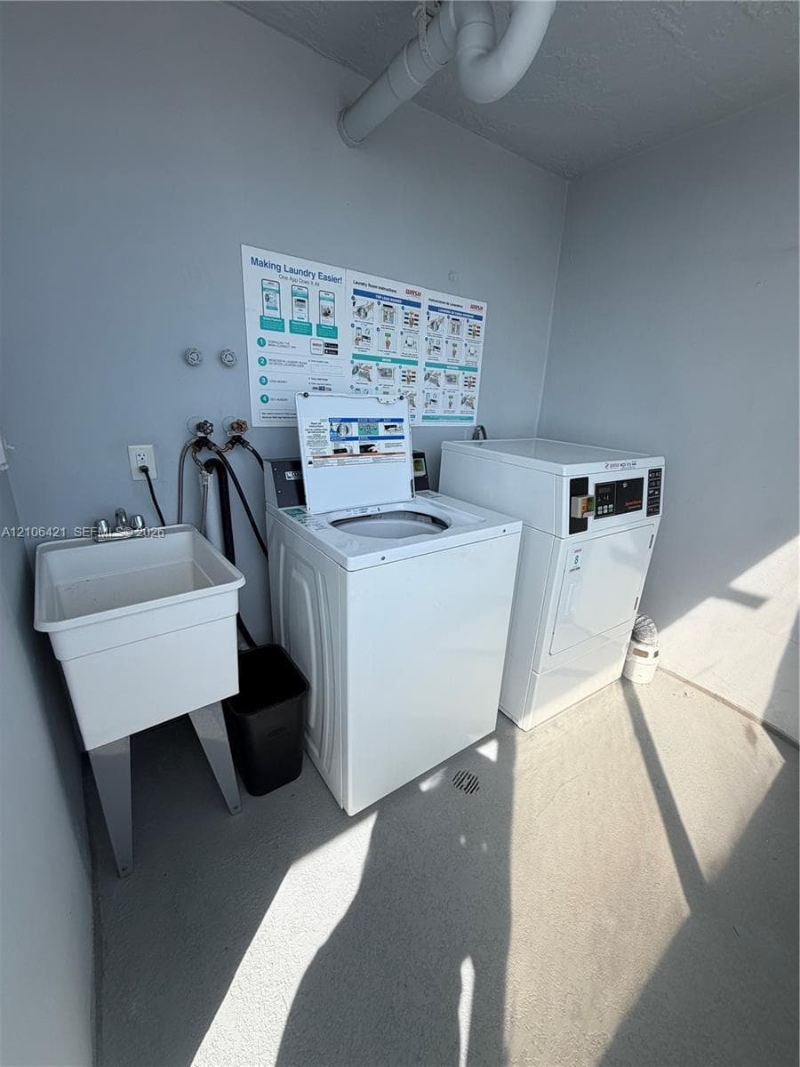 Laundry area featuring a utility basin with chrome faucet fixtures, top-load washer, dryer, and concrete flooring