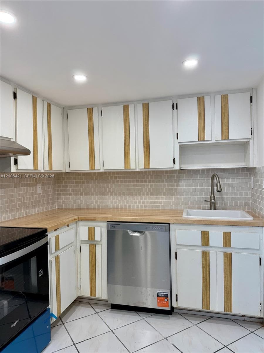 Kitchen featuring custom cabinetry with vertical wood accents, butcher block countertops, mosaic tile backsplash, stainless steel dishwasher, and recessed lighting