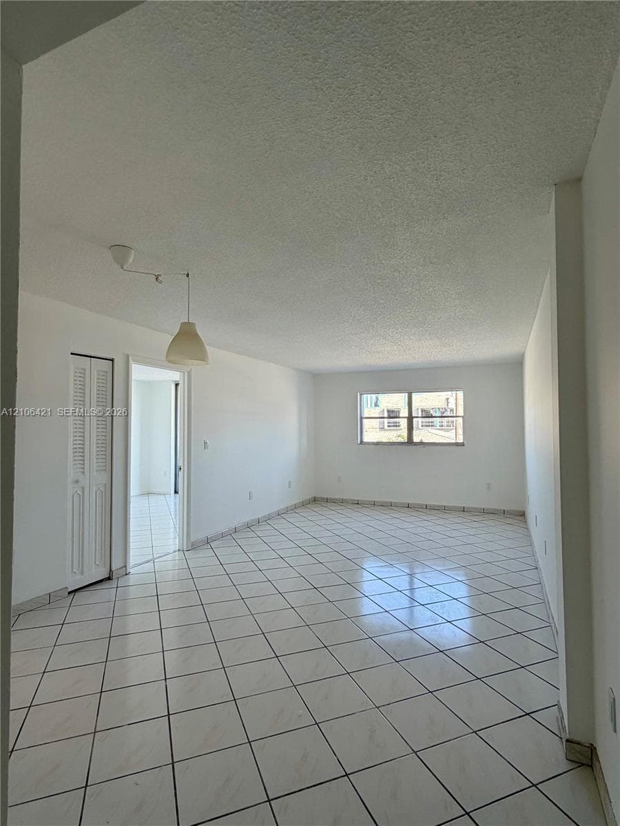 Open-concept interior featuring white floor tiles set in a diamond pattern, textured ceiling, pendant lighting fixture, and white louvered closet doors