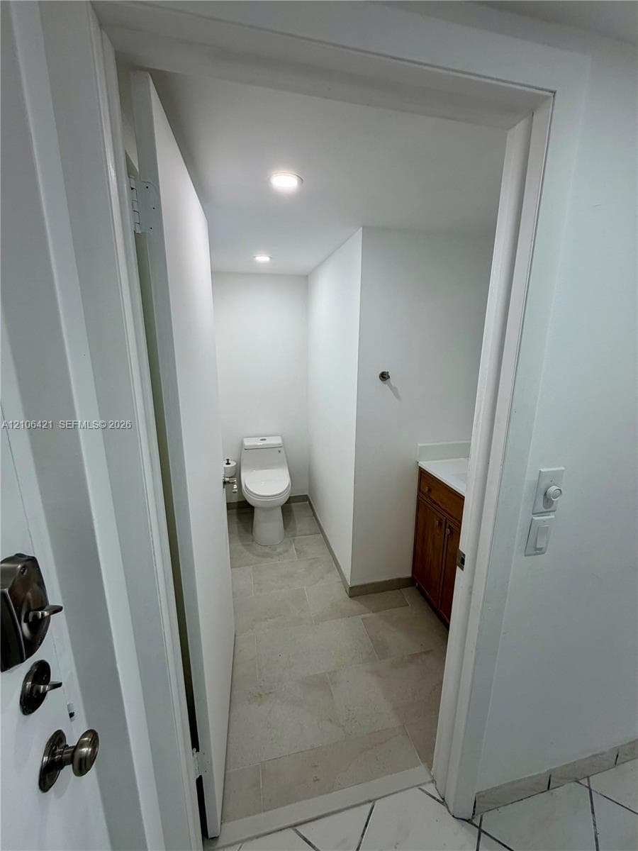 Restroom featuring a wood-finish vanity, stone-surface countertop, recessed lighting, and large-format tile flooring