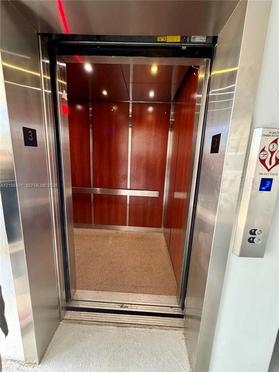 Elevator featuring wood-finish wall panels, stainless steel trim, recessed lighting, and a horizontal metal handrail