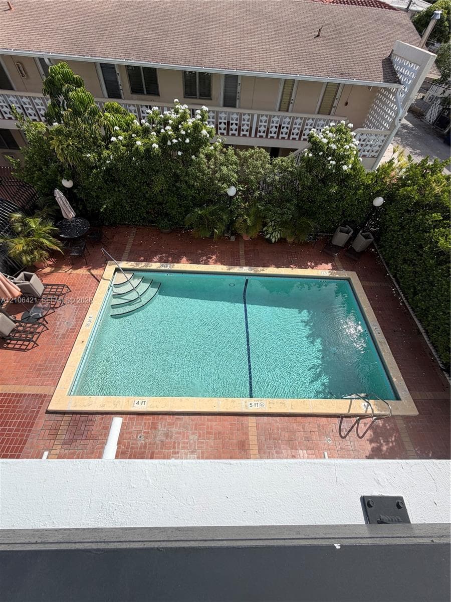 In-ground swimming pool with integrated stairs and metal handrails, surrounded by a brick-paved deck and privacy hedging