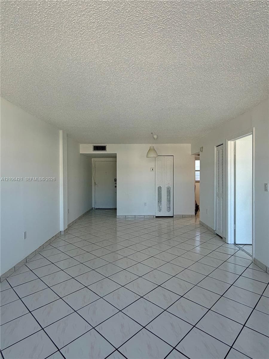Open floor plan featuring large-format diagonal tile flooring, white interior walls, and built-in closet cabinetry with louvered doors