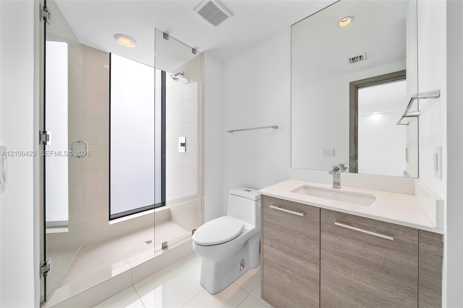 Full-height frameless glass shower enclosure with integrated window, wood-finish vanity with stone countertop, rectangular undermount sink, and polished chrome fixtures