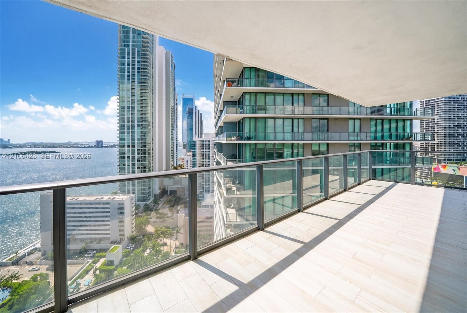 Expansive covered balcony featuring light-toned tile flooring and a glass panel railing