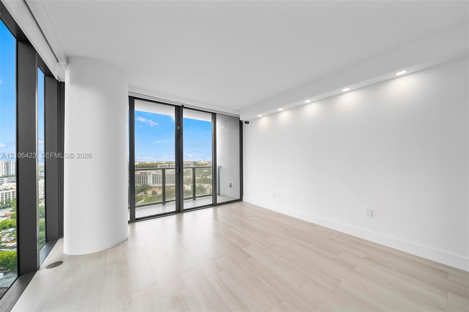 Floor-to-ceiling windows, wood-finish flooring, recessed ceiling lighting, and a private balcony featuring a metal railing