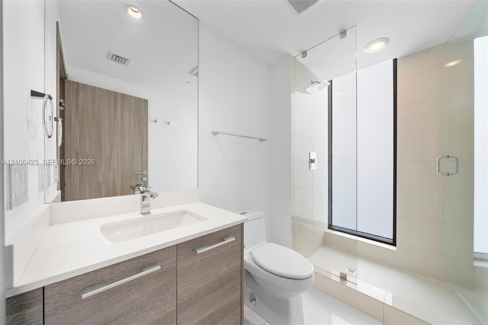 Bathroom featuring a floating wood-finish vanity with a white countertop, large frameless mirror, glass-enclosed walk-in shower with floor-to-ceiling tile, and recessed lighting