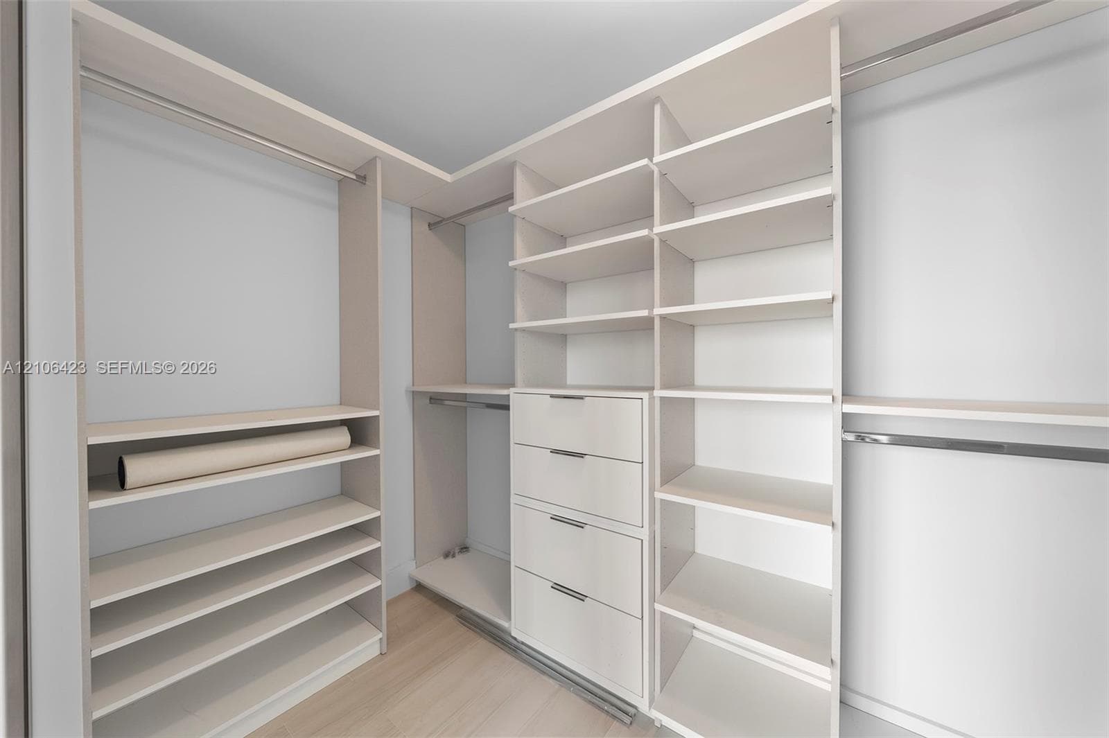 Custom walk-in closet featuring light-toned built-in cabinetry, floor-to-ceiling shelving, integrated hanging rods, and a multi-drawer dresser unit
