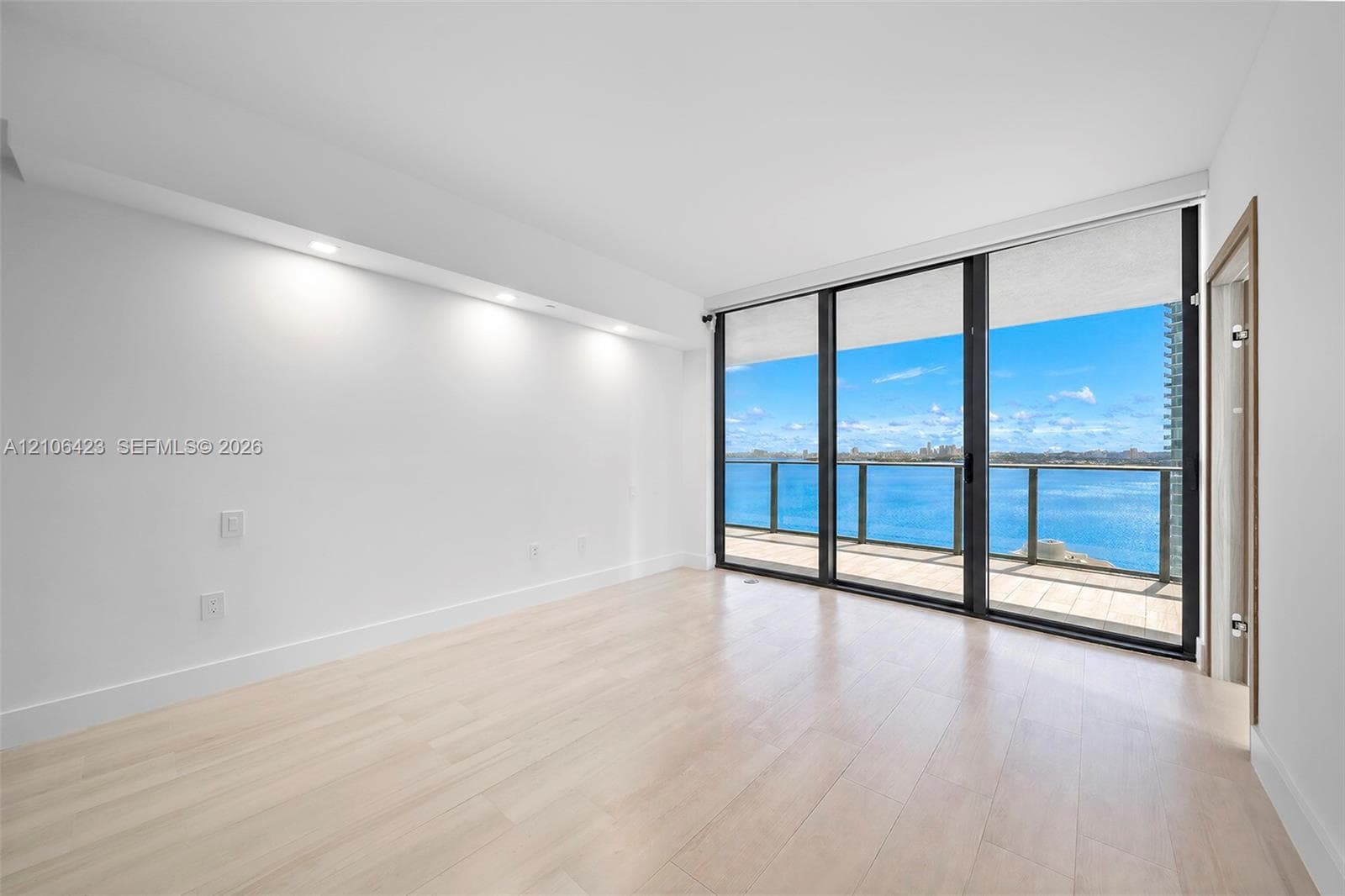 Floor-to-ceiling windows, wood-finish flooring, recessed ceiling lighting, and a private balcony featuring a water backdrop