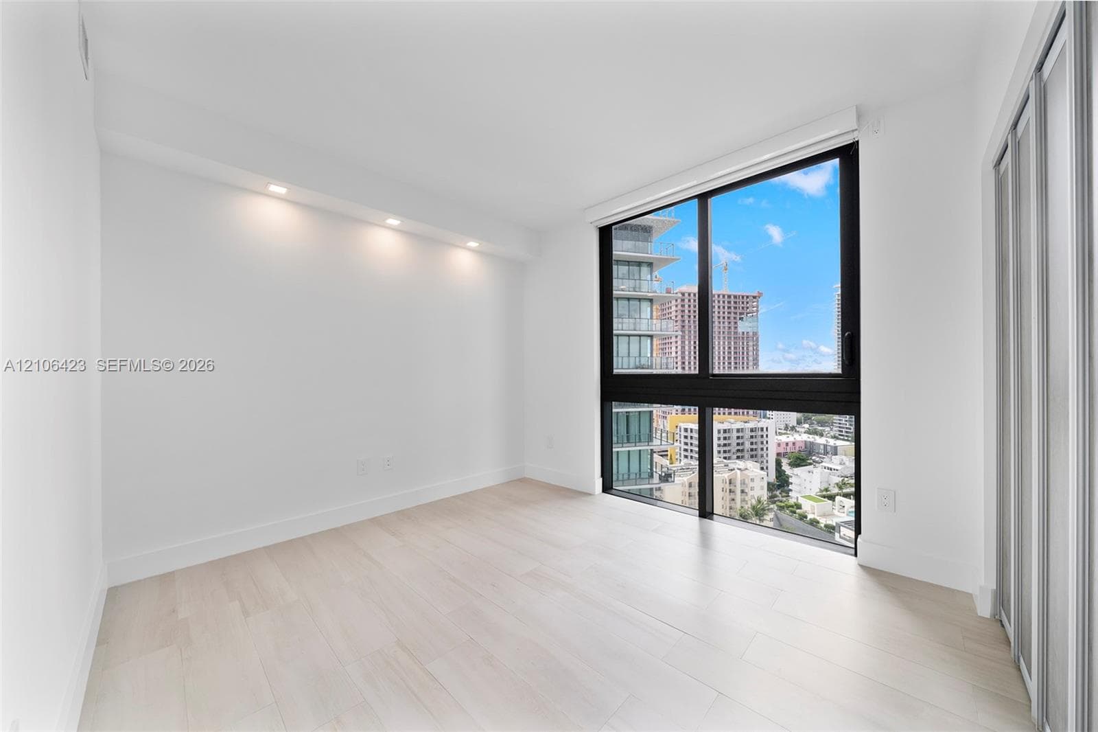 Light-filled room featuring floor-to-ceiling windows with black frames, wood-finish flooring, recessed architectural lighting, and floor-to-ceiling sliding closet doors