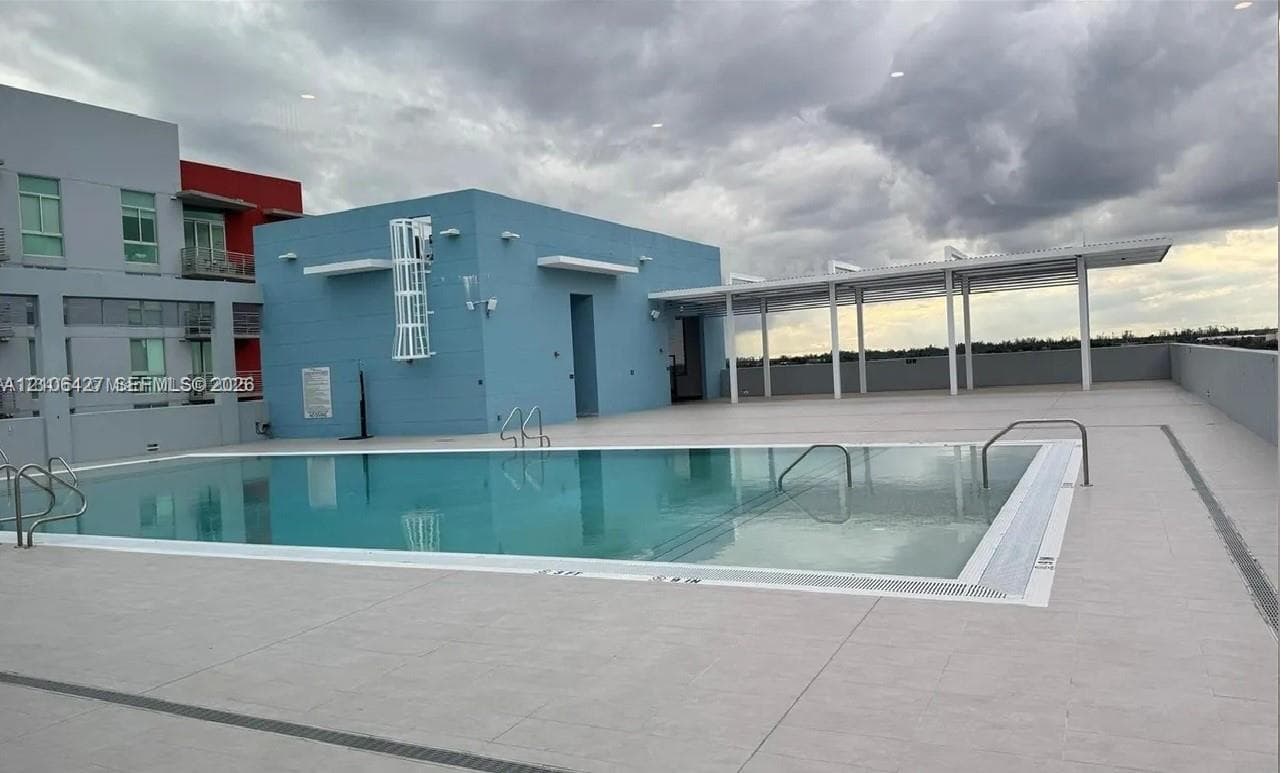 Rooftop swimming pool featuring a tiled deck, metal handrails, and a covered pergola area