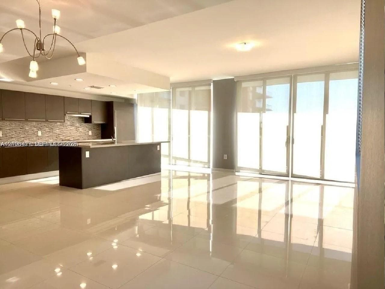 Contemporary kitchen featuring dark cabinetry, a central island, a multi-tonal stone tile backsplash, polished large-format floor tiling, and floor-to-ceiling glass panel doors