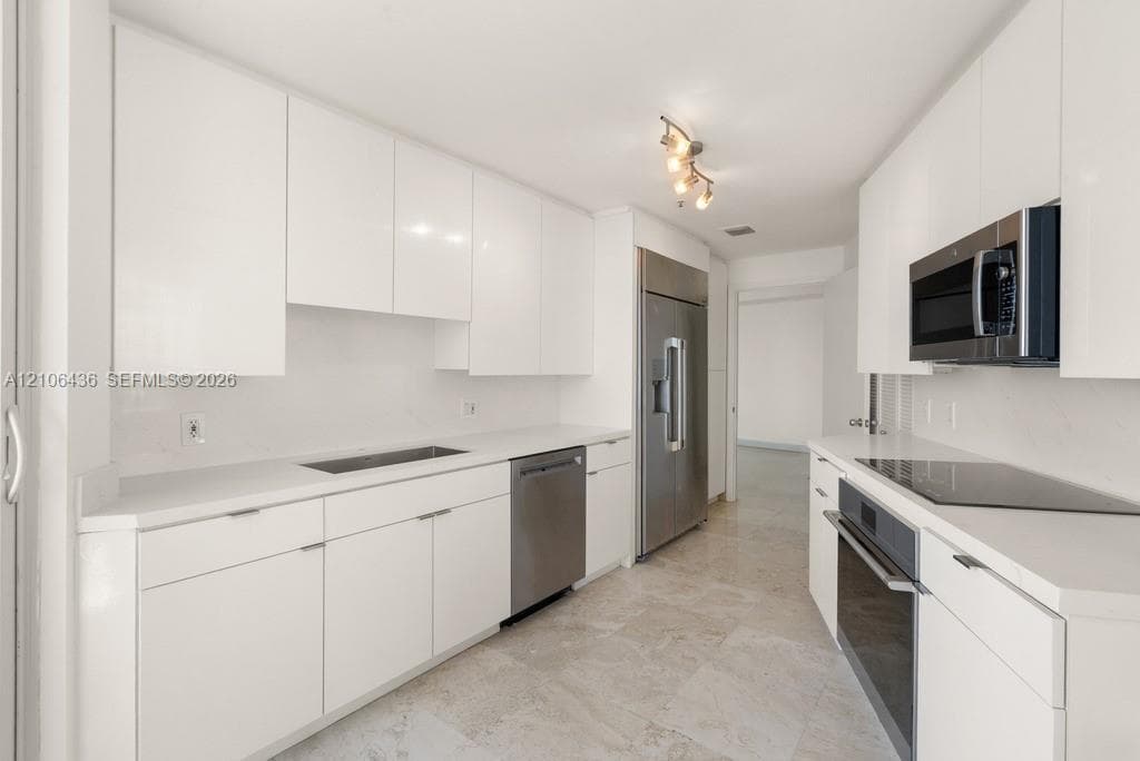 Kitchen featuring flat-panel white cabinetry, stone-surface countertops, full-suite stainless steel appliances, and stone tile flooring