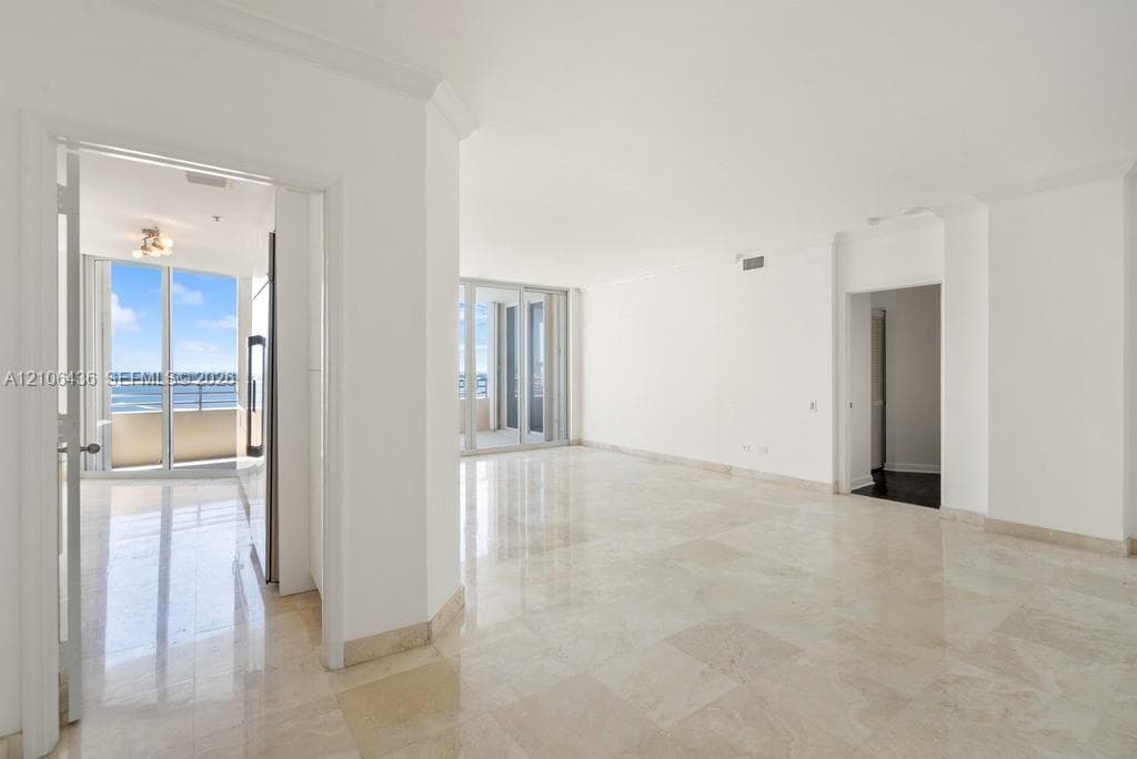 Open interior featuring polished stone flooring, crown molding, floor-to-ceiling glass sliding doors, and private balcony access