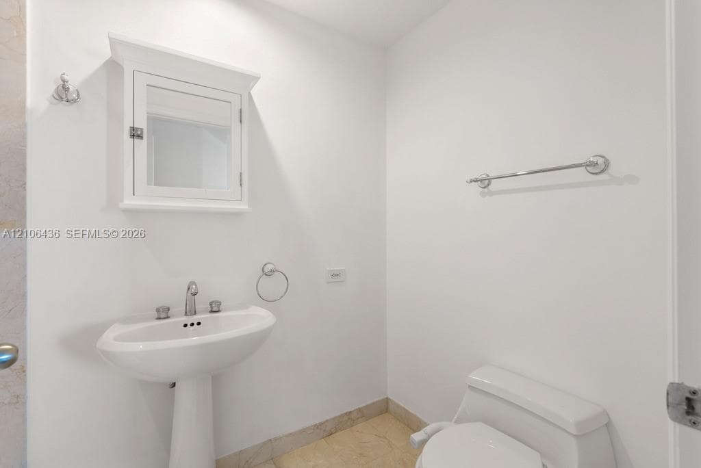 Pedestal sink with polished chrome fixtures, wall-mounted medicine cabinet with crown molding, and stone-finish flooring