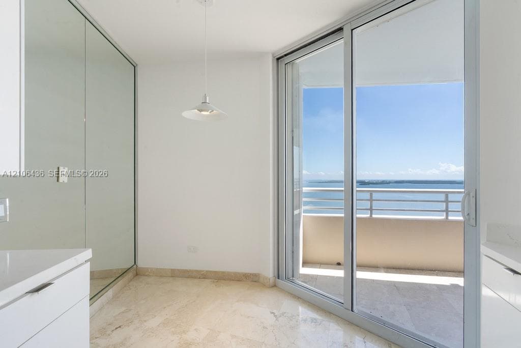 Floor-to-ceiling mirror paneling, stone flooring, minimalist pendant lighting, and full-height sliding glass doors opening to a balcony with water exposure