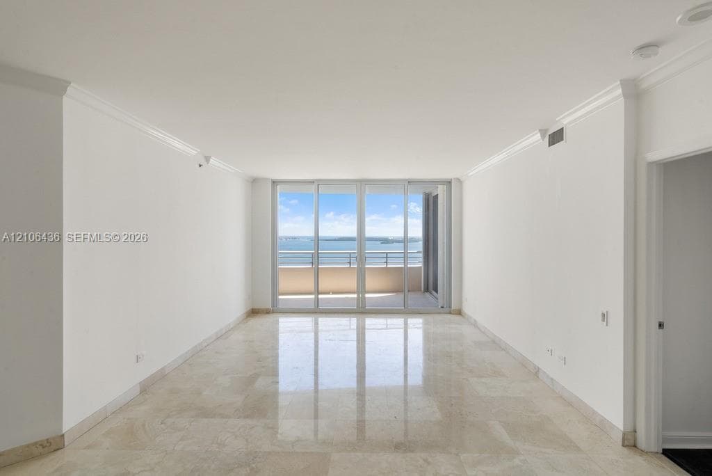 Living area featuring polished stone flooring, crown molding, and floor-to-ceiling glass sliding doors opening to a private balcony